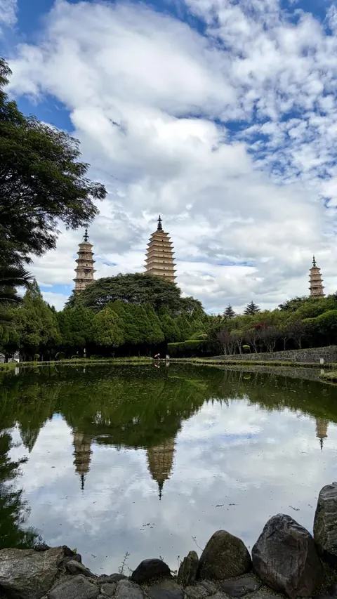 The Three Pagodas mirrored in the reflecting pool under a cloudy sky